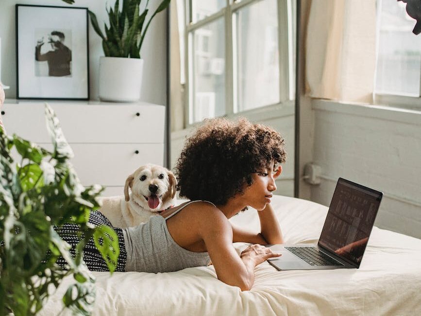 relaxed black woman watching laptop near dog on bed