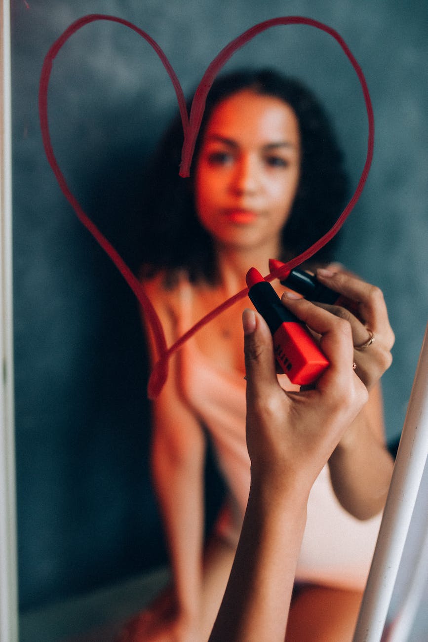 a woman holding red lipstick while looking at the mirror